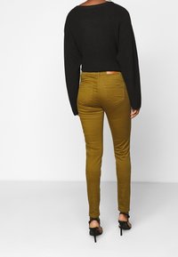 Oliwkowe wąskie dżinsy o gładkiej fakturze, połączone z luźnym czarnym swetrem. Posiadają tylne kieszenie i widoczny pas.