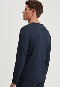 Navy langarmshirt met ronde hals, gemaakt van gladde stof, met een klein logo-detail op de achterkant. Schoon design en nauwsluitende pasvorm.