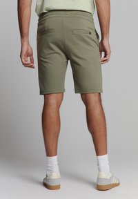 Khaki shorts met een gladde textuur, met daarachter twee zakken. Gecombineerd met grijze schoenen en witte sokken, weergegeven van achteren.