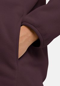 Korte paarse fleece kledingstuk met een verborgen zak aan de manchet en elastische afwerking. Zachte textuur en gladde afwerking zichtbaar.