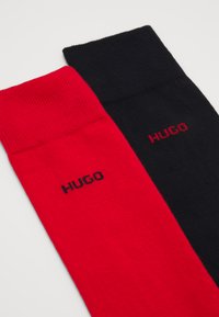 Calcetines de algodón rojos y negros con puños acanalados; logo "HUGO" en colores contrastantes en cada calcetín. Textura suave y longitud estándar.