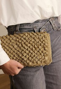 Geweven clutch tas in goud, met een gestructureerd, geknoopt ontwerp. Het materiaal lijkt een synthetische of natuurlijke vezel te zijn. Compacte vorm.