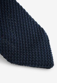 Corbata de punto azul marino con un patrón texturizado, que se estrecha hasta un extremo puntiagudo. El material parece resistente pero flexible.