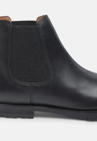 Stivale alla caviglia in pelle nera con pannelli laterali elastici, accenti in tessuto testurizzato e suola in gomma resistente. Design minimalista, finitura liscia.