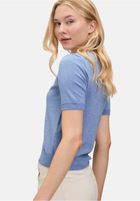 Maglione azzurro chiaro a maniche corte lavorato a maglia con un design aderente. Presenta un colletto e polsini a coste, con una lieve lucentezza e un dettaglio del logo sull'orlo.