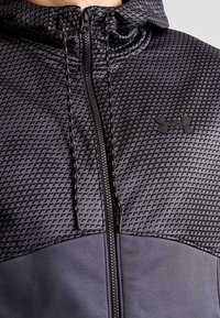 Felpa nera con zip, pannello superiore a fantasia, materiale testurizzato, cordini regolabili e logo sul lato destro. Tessuto impermeabile.