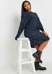 Robe longue à manches longues imprimé léopard marine, fabriquée en tissu doux, avec une coupe décontractée et des poches latérales. Associée à des bottes de combat noires à lacets.