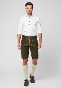 Pantaloni lederhosen corti di un verde scuro con modelli floreali ricamati, abbinati a una camicia bianca con colletto e calze color crema fino al ginocchio. Scarpe marroni.