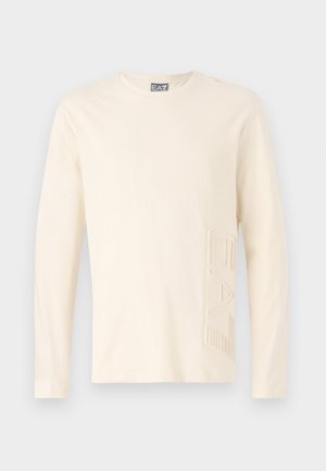T-shirt crème à manches longues en coton doux, avec un logo EA7 texturé sur le côté gauche devant. Col rond simple.