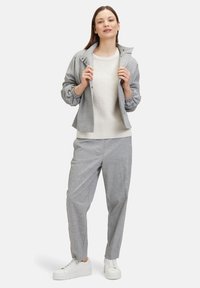 Hellgraue Jacke mit elastischen Bündchen, weißem geripptem Pullover und passenden grauen Hosen. Kombiniert mit weißen Sneakern. Einfacher, lässiger Schnitt.