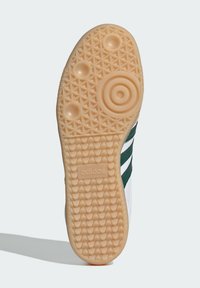 Suola bianca di una scarpa con fondo in gomma gommata testurizzata, caratterizzata da motivi circolari e triangolari. Logo "adidas" impresso vicino al tallone.