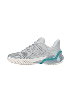 Chaussure de sport gris clair avec motifs chevrons texturés, accents turquoise sur le soutien du talon et semelle blanche à rainures pour l'adhérence.