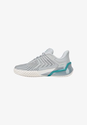 Chaussure de sport gris clair avec motifs chevrons texturés, accents turquoise sur le soutien du talon et semelle blanche à rainures pour l'adhérence.