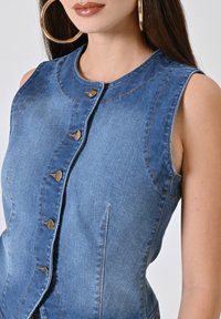 Gilet in jeans con un design aderente, tessuto in denim azzurro chiaro, bottoni color oro e dettagli di cucitura a vista. Senza maniche e con tasche laterali.