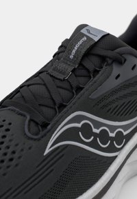 Black athletic shoe with mesh upper, laces, and Saucony logo. Features a textured design and white midsole with subtle detailing.