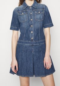 Vestido de camisa de mezclilla, mangas cortas, lavado azul oscuro, cierre de botones, dos bolsillos en el pecho, falda con plisados, detalles de dobladillo deshilachado.