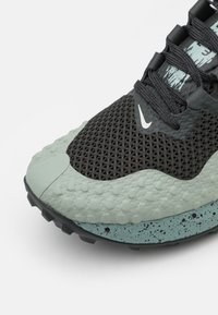 Sneakers Nike z siateczkową cholewką w kolorze czarnym, z fakturowanymi zielonymi akcentami, zakrzywioną podeszwą w odcieniu miętowym i czarnymi gumowymi wbitymi kołkami.
