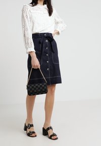 Biała haftowana bluzka z długimi rękawami, granatowa spódnica z guzikami i paskiem do wiązania, czarna kraciasta torebka oraz czarne sandały na obcasie.