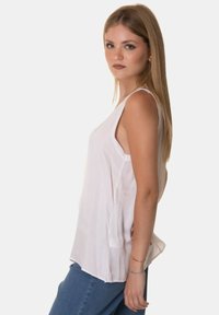 Blusa bianca senza maniche in un tessuto leggero e liscio; vestibilità rilassata con orlo curvo e spaccature laterali; indossata con jeans blu.