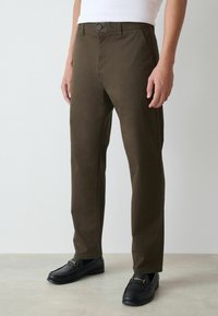 Olive zaļas bikses ar šauru piegriezumu, izgatavotas no kokvilnas un sintētisku šķiedru maisījuma; tām ir pogu aizdare, slīpi sānu kabatas un gluda tekstūra.