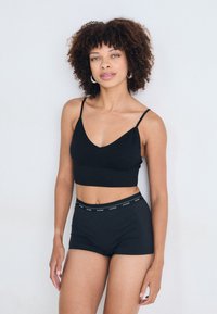 Crop top noir sans couture avec bretelles fines ajustables et short noir avec une ceinture élastique à logo. Texture lisse et design ajusté.