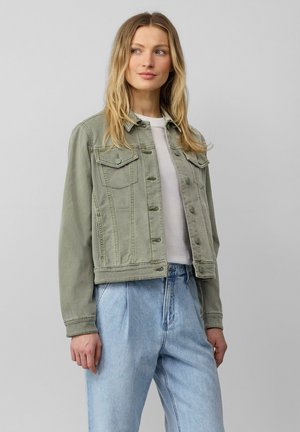 Hellgrüne Jeansjacke mit cropped Schnitt, Knopfleiste, zwei Brusttaschen und leicht distressed Textur, kombiniert mit hellblauen Hosen.