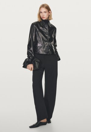Černá kožená bunda s lesklým povrchem, velkým límcem a předními knoflíky. Kombinováno s černými širokými nohavicemi a strukturovanou kabelkou do ruky.