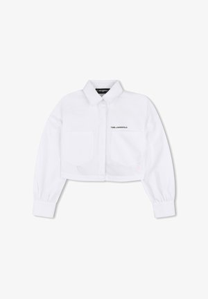 Chemise blanche raccourcie en coton avec manches longues, fermeture boutonnée à l'avant, deux poches devant et détail de logo visible sur le côté gauche.