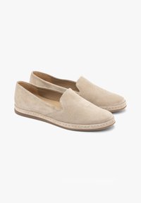 Para beżowych zamszowych mokasynów na płaskiej gumowej podeszwie z niskim obcasem i widocznym przeszyciem wokół krawędzi na białym tle.