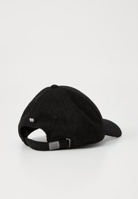 Casquette en velours côtelé noir avec une visière incurvée, une sangle réglable et un petit texte blanc "85" à l'arrière. Surface texturée avec des ridges verticaux.