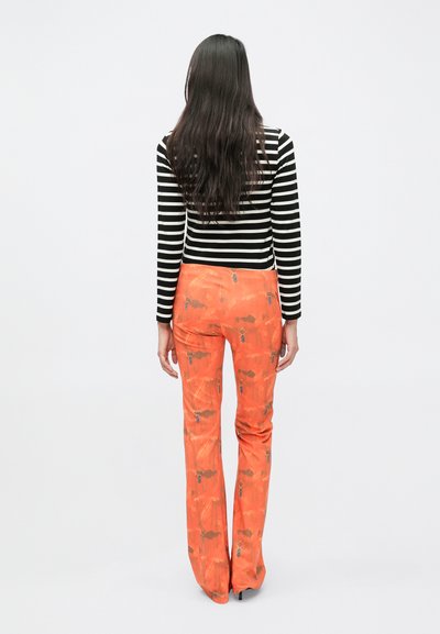 Melns un balts svītrains garroku tops kopā ar izplatītām oranžām biksēm ar ziedu rakstu un metāla akcentiem.