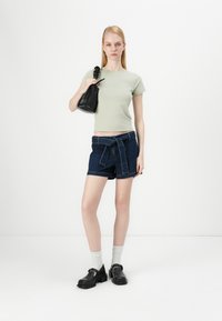 Light green fitted t-shirt, dark denim shorts with bow tie detail, black handbag, white socks, and black chunky shoes. Simple, casual look.