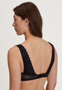 Zwarte kant bralette met een V-vormige achterkant, geschulpte bandjes en haaksluiting. Bevat een bloemenpatroon en een gestructureerde stof.