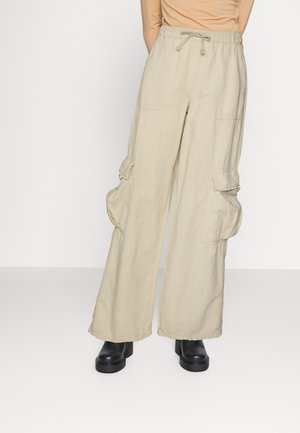 Μπεζ καμπάνες cargo από ελαφρύ ύφασμα, με ελαστική μέση, κορδόνι και πολλές μπροστινές τσέπες. Φοριούνται με μαύρες πλατφόρμες μποτίνια.