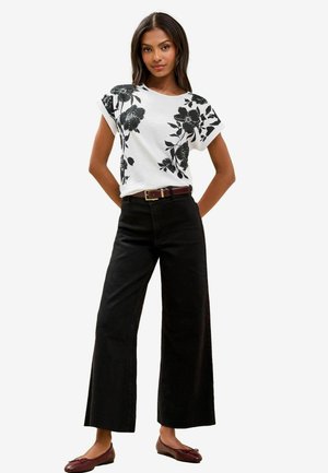 T-shirt bianco con stampa floreale e maniche arrotolate, abbinato a pantaloni a gamba larga neri e ballerine borgogna. Tessuto morbido e vestibilità rilassata.