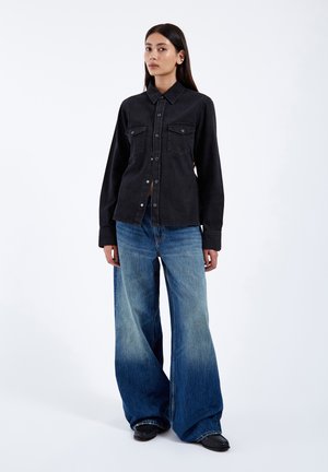 Černá džínová košile s límcem a knoflíkovým zapínáním, v kombinaci s modrými džíny s širokými nohavicemi a gradientním efektem. Jednoduchý design, bez viditelných vzorů.