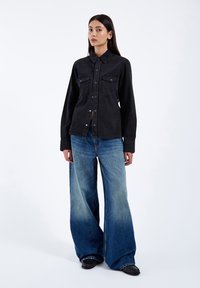 Black denim shirt with a collar and button closure, paired with wide-leg gradient blue jeans. Simple design, no visible patterns.