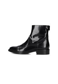 Gepolijste zwarte leren enkellaars met lage hak, brogue-details en knoopriem aan de zijkant op een witte achtergrond.