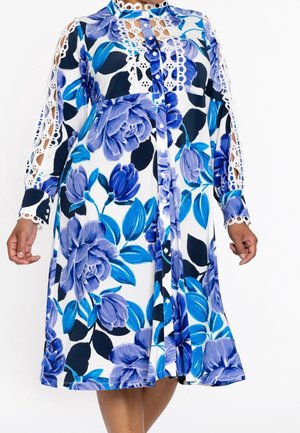 Long-sleeve white dress with large blue floral print, button-down front, and lace cutout details on sleeves and upper chest.