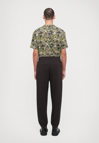 Floral-patterned short-sleeve shirt in green, yellow, and brown tones paired with black tapered pants and black footwear.