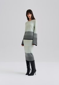 Ensemble en tricot en deux pièces couleur vert menthe avec des accents de motifs géométriques noirs, présentant de longues manches en cloche et une silhouette ajustée.