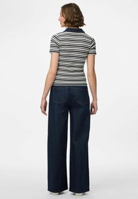 Randig polo skjorta i marinblått och vitt, i kombination med vida mörka jeans. Har en ribbad textur och klassisk krage.