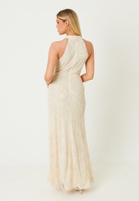 Beige Abendkleid mit aufwendiger Perlenstickerei und floralen Mustern, hohem Kragen, ärmellosem Design und fließender Silhouette.