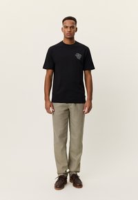 Μαύρο βαμβακερό μπλουζάκι με κοντά μανίκια, με γραφικό στο στήθος. Συνδυάζεται με ανοιχτό μπεζ παντελόνι και καφέ δερμάτινα παπούτσια με κορδόνια.