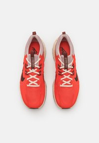 Coppia di scarpe da corsa Nike di un rosso acceso con lacci bianchi e suole beige, viste dall'alto su sfondo bianco.