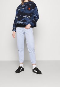 Mörkblå camouflagemönstrad sweatshirt med svart fåll, tillsammans med ljusblå uppvikta joggers och svarta sneakers med vita ränder.