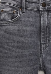 Gros plan de jean en denim gris de face avec ceinture, fermeture éclair, bouton, poches avant et poche monnaie avec rivets métalliques.
