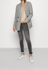 Blazer de cuadros gris de doble botonadura, suéter de punto beige, jeans skinny gris oscuro y zapatillas blancas con detalles verdes.