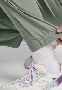 Lichtgroene, loszittende sportbroek met elastische boorden, gecombineerd met witte geribde sokken en crèmekleurige sneakers met lila accenten.