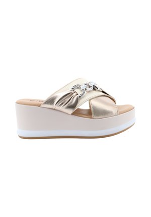 Sandalo con zeppa beige con cinturini incrociati in metallo oro e dettaglio decorativo con catena argento su sfondo bianco.